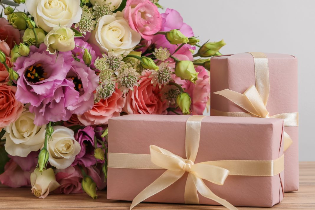 Beautiful bouquet of flowers and gift boxes on wooden table agai